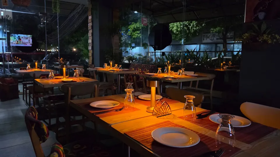 Mesas de la terraza de T’chaka con luz cálida y plantas por la noche